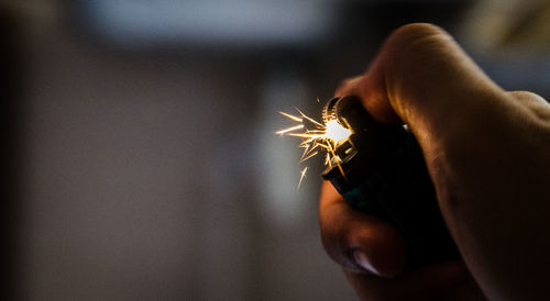 Cropped hand igniting cigarette lighter in darkroom