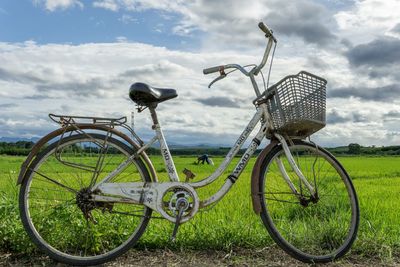 Bicycle parked in basket on field against sky
