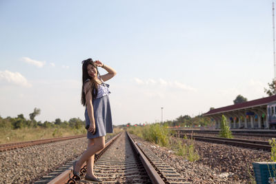 Side view of woman standing on railroad tracks against sky