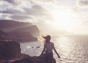 Rear view of woman standing by sea against sky