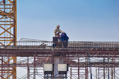 Low angle view of people standing on bridge against clear sky