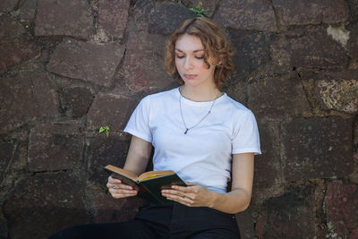 Full length of young woman reading book against wall
