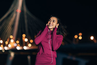 Portrait of smiling woman standing against illuminated city at night