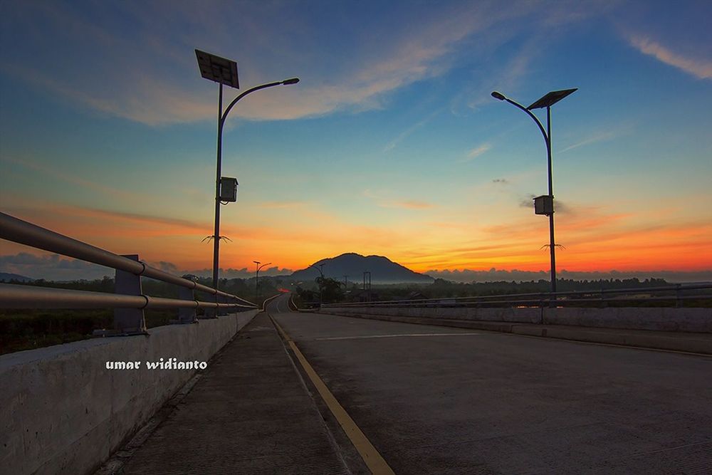 the way forward, street light, sunset, sky, lighting equipment, diminishing perspective, road, vanishing point, orange color, transportation, empty, cloud - sky, street, road marking, lamp post, cloud, long, road sign, tranquility, in a row