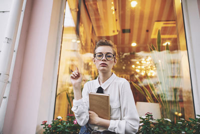 Portrait of young woman using mobile phone while standing in office