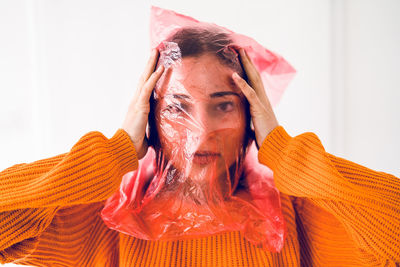 Portrait of teenage girl face covered with plastic bag standing against wall at home