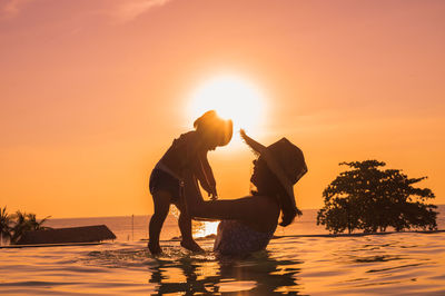Silhouette people on shore against sky during sunset