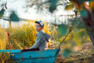 Boy looking away while sitting on land