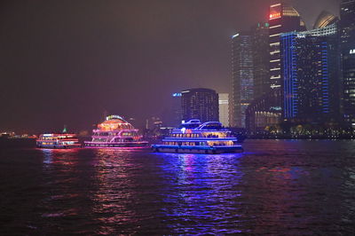 Illuminated modern buildings by sea against sky at night