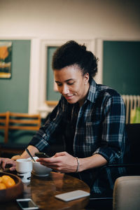 Smiling businessman using mobile phone while having food at table in creative office