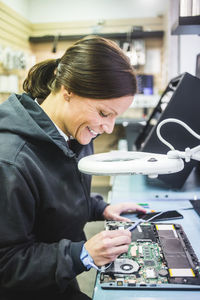 Side view of smiling mature technician working on computer part in workshop