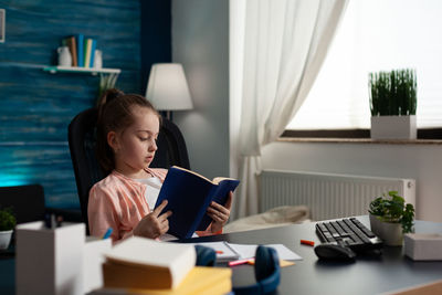 Cute girl reading book while sitting at office