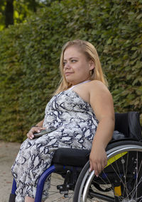 Young pretty woman with short height on wheelchair enjoys time in green park at summer day. smiling