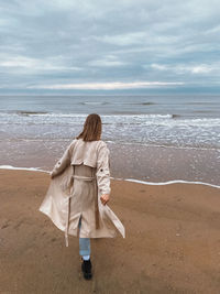 Rear view of woman standing on beach against sky and sea