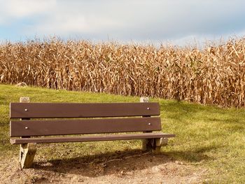 Empty bench on field against sky