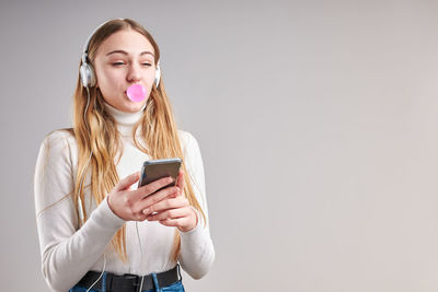 Teenage girl bowing chewing gum while standing against gray background