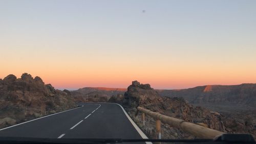 Road leading towards mountains against clear sky during sunset