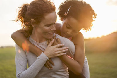 Mother giving piggyback to daughter at park during sunset