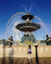 Girl standing by fountain against sky