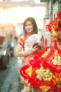 Full length of smiling woman holding hand fan standing at street