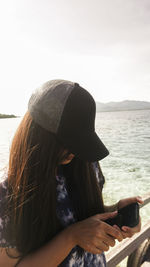 Man using mobile phone while sitting on sea against sky