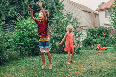 Siblings playing with sprinkler at yard