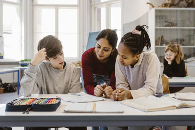 Teacher discussing with male and female students sitting at desk in classroom