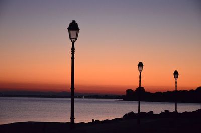 Street light by sea against orange sky