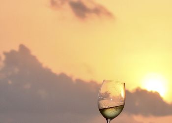 Close-up of wineglass against sky during sunset