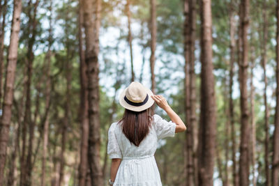 Rear view of woman standing against trees in forest