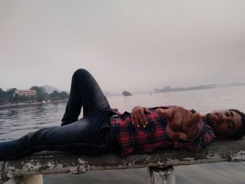 Portrait of young man lying down against sky