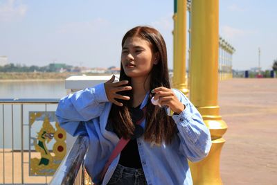 Beautiful woman standing by pole gesturing while standing against sky