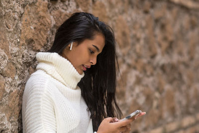 Beautiful brunette young woman in winter clothes using smartphone listening to music with earphones