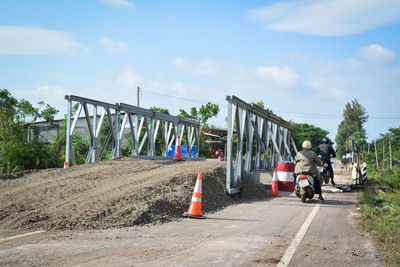 Rear view of people riding vehicles by incomplete bridge on road