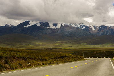 Country road leading towards mountains against sky