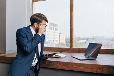 Side view of young man using laptop while standing in office