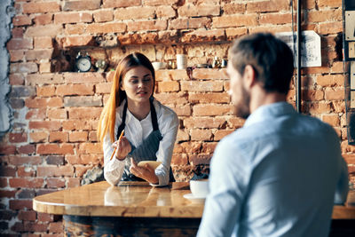 Young couple sitting at restaurant against brick wall