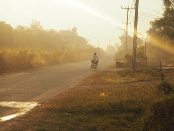 Man riding bicycle on road amidst field against sky