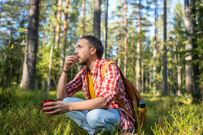 Side view of man using mobile phone while sitting in forest