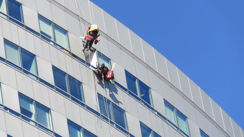 Low angle view of people working on modern building against blue sky