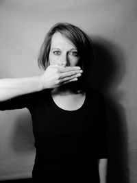 Portrait of woman covering mouth while standing against wall