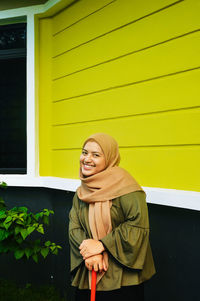 Portrait of a smiling young woman standing against wall