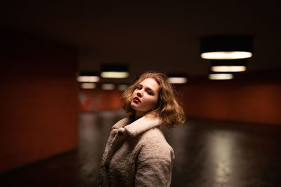 Young woman looking away while standing in illuminated room