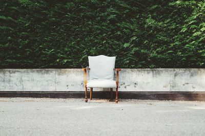 Wooden armchair on street in front of lush green leaves