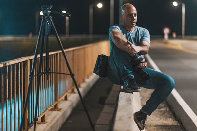 Man holding camera sitting by railing at night