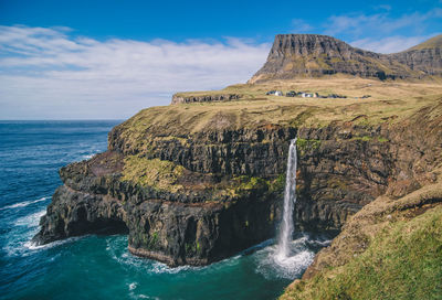 Scenic view of waterfall on rock formation by sea against sky