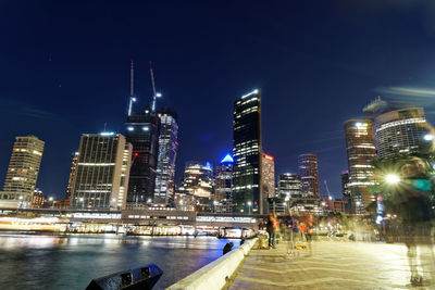 Illuminated buildings by river against sky in city at night