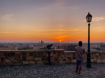 Rear view of people on street by buildings against sky during sunset