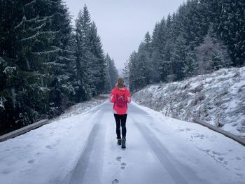 Woman hiking alone on an empty road surrounded by coniferous trees and leaving footprints behind