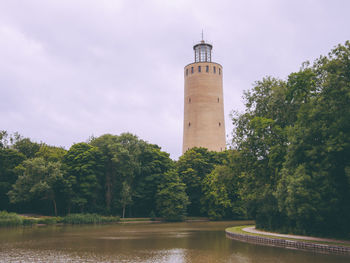 Lighthouse amidst trees and buildings against sky